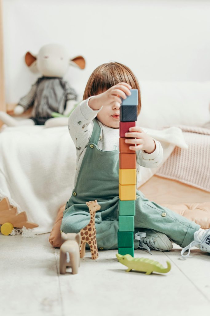 Un enfant mignon empile des blocs de bois colorés tout en jouant à l'intérieur, entouré de jouets.