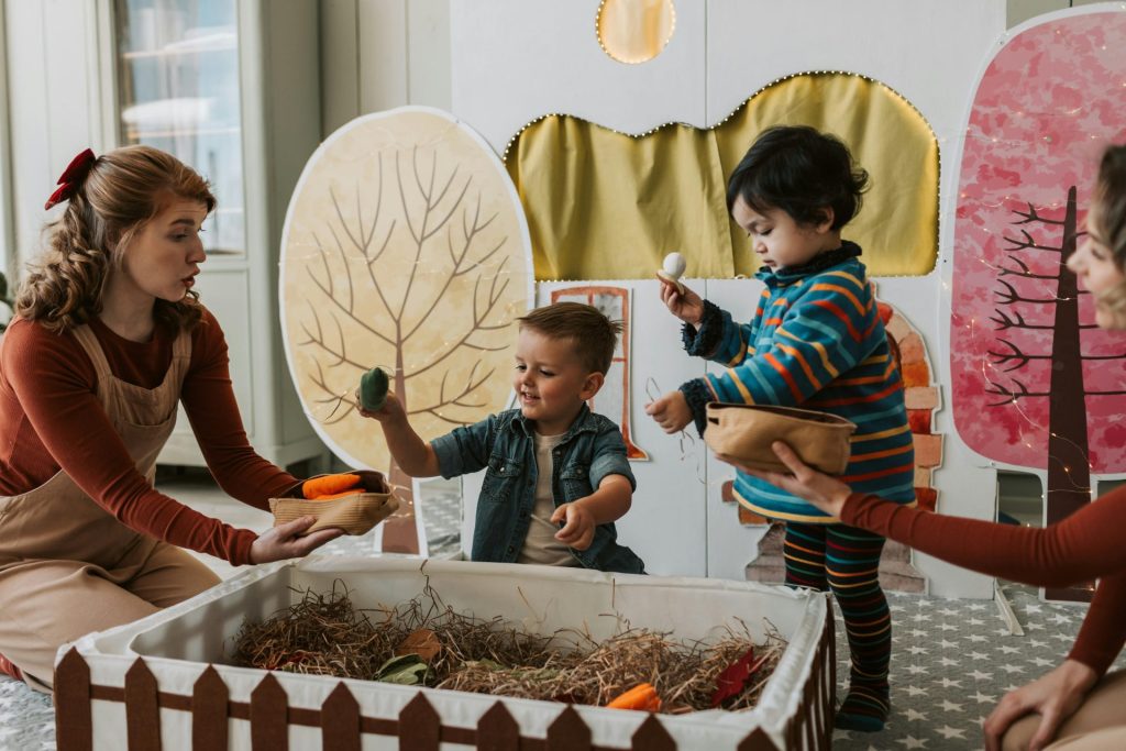 Deux enfants et une femme jouent avec des marionnettes à l'intérieur, profitant d'un jeu créatif avec un décor sur le thème de la nature.